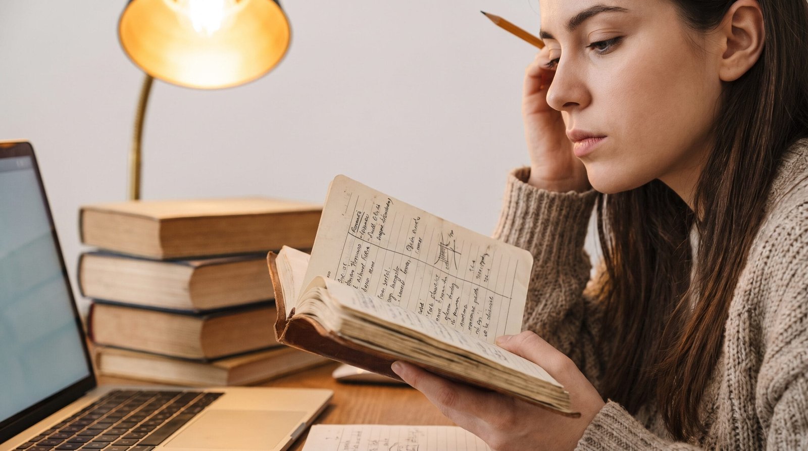 Female student holding a handwritten student daily planner while studying with a laptop and textbooks on a wooden desk.